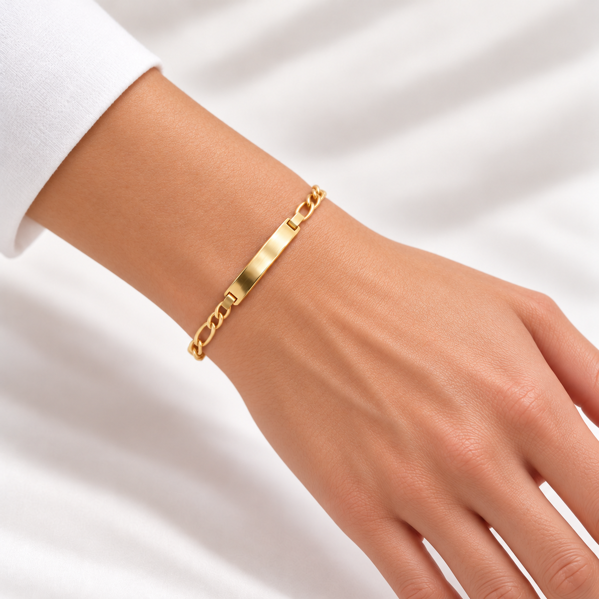 Figaro-Armband aus 585 Gelbgold mit polierter Gravurplatte an einem Damenhandgelenk getragen.
