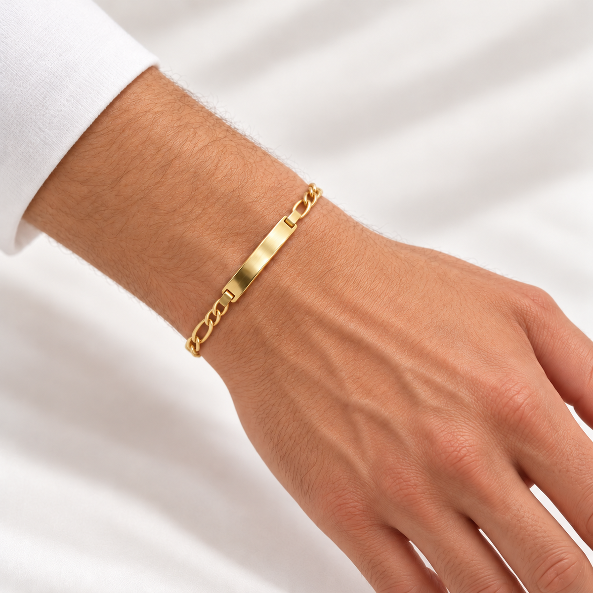 Figaro-Armband aus 585 Gelbgold mit länglicher Gravurplatte an einem Herrenhandgelenk getragen.