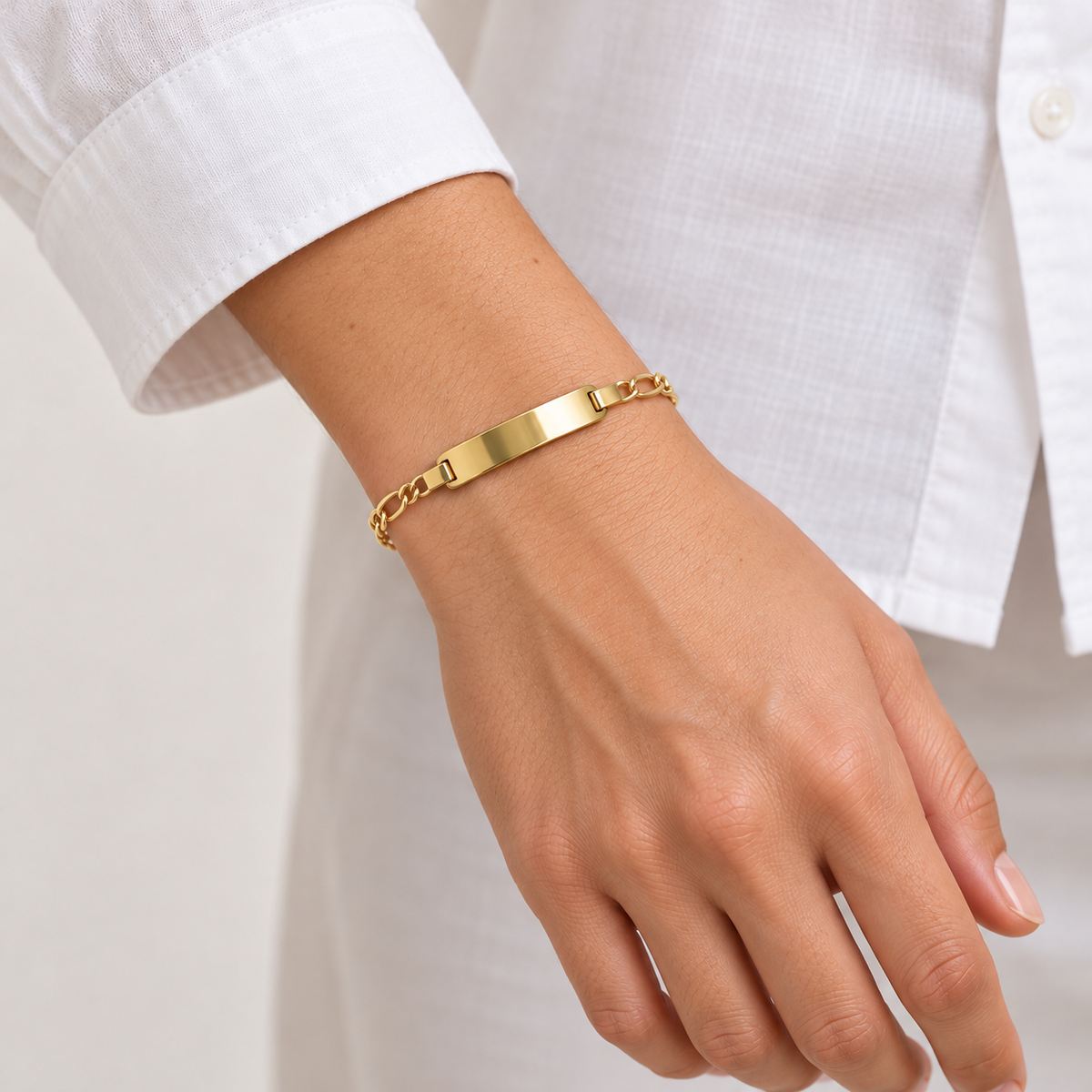 Figaro-Armband aus 585 Gelbgold mit polierter Gravurplatte an einem Damenhandgelenk getragen.