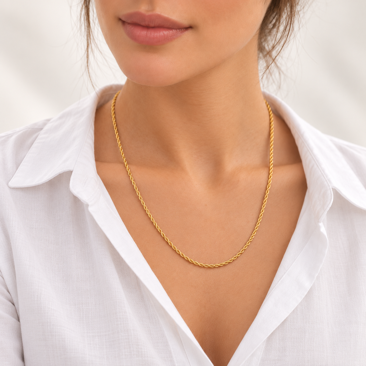 Frau mit weißer Bluse trägt eine feine Kordelkette aus 585 Gelbgold ohne Anhänger am Dekolleté.